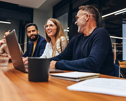 Employees sitting at a office table smiling in front of a laptop